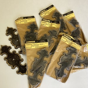 May include: Eight antique brass cabinet hardware backplates in individual packaging. Each backplate features a decorative, ornate design with a single mounting hole. The packaging is labelled "Onward Cabinet Hardware" and includes the product number "NT171-AB" and the finish "Antique Brass Finish."