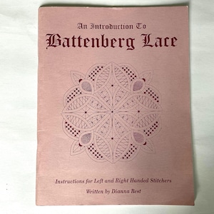 May include: A vintage pink book titled "An Introduction To Battenberg Lace." The cover features a detailed burgundy lace design and text. The book includes instructions for left and right-handed stitchers, written by Dianna Best.