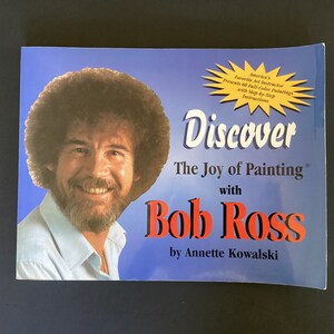 May include: Book cover featuring a portrait of Bob Ross, with the title "Discover The Joy of Painting with Bob Ross" and the author "by Annette Kowalski".