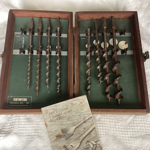 May include: A vintage set of Irwin wood bits in a wooden case. The case is open, revealing several bits of varying sizes and shapes. A booklet titled "How to Select, Use and Care for Wood Bits" is in the foreground. The case has a green interior.