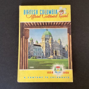 May include: A yellow book with the title "British Columbia Official Centennial Record" and the text "Fort Langley 1858" and "1858 1958 A Century to Celebrate". The book features a picture of the British Columbia Parliament Buildings.