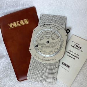 May include: A Telex E-6B flight computer model FDF-57 with a circular slide rule, a rectangular grid base, a brown leather storage case with the Telex logo, and an instructional manual titled How to Use Your Telex E-6B Computer FDF-51A/57/60.