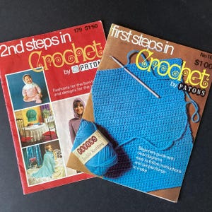 May include: Two vintage Patons crochet instruction booklets. The red booklet titled 2nd steps in Crochet features photos of a child in a pink outfit and a person in a hooded sweater. The brown booklet titled first steps in Crochet includes a blue yarn skein and a crochet hook.