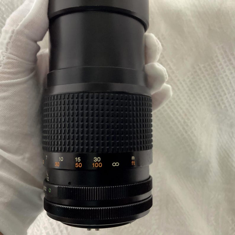 May include: A black camera lens with a textured grip and distance markings. The lens has a series of numbers indicating focal lengths, including 30, 50, and 100, and a measurement scale in feet.