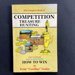 May include: A yellow book titled "The Complete Book of Competition Treasure Hunting" with a cartoon illustration of a person holding a metal detector and a trophy cup. The book cover features multiple photos of people participating in a treasure hunt.