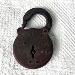 May include: A vintage, rusty brown padlock with the text "UNION" and "ACHIEVER" engraved on its surface. The lock is open, revealing the keyhole. The padlock is circular with a curved top and is set against a white, textured background.