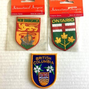 Peut inclure: Trois écussons brodés représentant des emblèmes provinciaux. Les écussons supérieurs sont étiquetés "New Brunswick" et "Ontario", avec l'écusson "British Columbia" en dessous. Chaque écusson a un design et une palette de couleurs uniques, avec le texte "British Columbia".