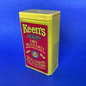 May include: A yellow rectangular tin of Keen's Dry Mustard. The tin has a red label with white and yellow text, including "DRY MUSTARD" and "MOUTARDE EN POUDRE". The tin is on a blue background.