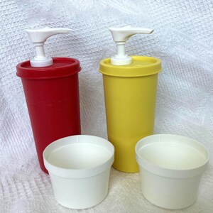 May include: A red and a yellow plastic pump dispenser with white pump heads and two white small containers. The dispensers are cylindrical and have a classic design. The containers are round and white.