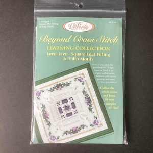 May include: A sealed plastic package containing a cross-stitch learning kit. The kit features the title "Beyond Cross Stitch" and includes instructions for square filet filling and tulip motifs. The design includes a floral pattern.