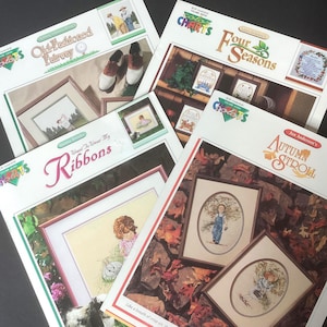 May include: Several cross-stitch pattern booklets are displayed, showcasing framed artwork. Titles include "Old-Fashioned Fairway," "Four Seasons," "Want to Wear My Ribbons," and "Autumn Stroll." The booklets feature designs of children and landscapes.