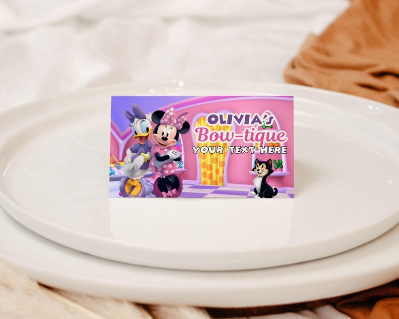 May include: A rectangular card featuring Minnie Mouse, Daisy Duck, and a black cat. The card has the text "OLIVIA'S Bow-tique" and "YOUR TEXT HERE" on a pink background. The card is on a white plate.