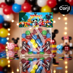 May include: Clear cellophane bags filled with colorful candies, topped with a banner featuring Mickey Mouse and friends. The banner reads "Thomas's 1st Birthday". Balloons in red, blue, black, and yellow are in the background.