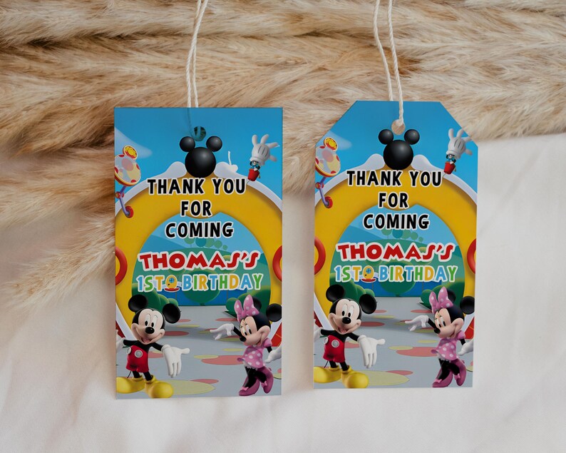 May include: Two birthday gift tags featuring Mickey and Minnie Mouse. The tags have a blue sky background with the text "Thank You For Coming" and "Thomas's 1st Birthday". The tags are rectangular and have a string attached.