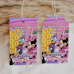 May include: Two pink and purple gift tags with the text "THANK YOU FOR COMING" and "OLIVIA'S Bow-tique". The tags feature cartoon images of Daisy Duck, Minnie Mouse, and a black cat.