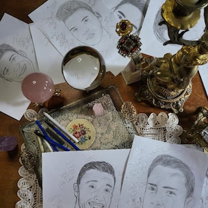 May include: A table with several pieces of paper featuring pencil drawings of people's faces. The drawings are surrounded by various decorative items, including a crystal ball, a candle holder, and a small tray with pencils.