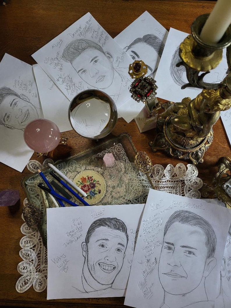 May include: A table with several pieces of paper featuring pencil drawings of people's faces. The drawings are surrounded by various decorative items, including a crystal ball, a candle holder, and a small tray with pencils.