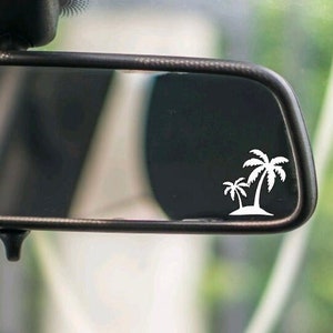 May include: A rearview mirror with a white palm tree sticker on the glass. The sticker is a simple design with two palm trees and a small island.