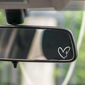 May include: A rearview mirror with a white heart with a cross inside on the glass. The heart is a simple line drawing.