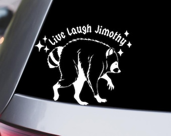 May include: A white vinyl decal applied to a car window featuring a silhouette of a raccoon in a hunched posture. Above the raccoon, the text reads Live Laugh Jimothy in a stylized font, accented by four-pointed star shapes on both sides.