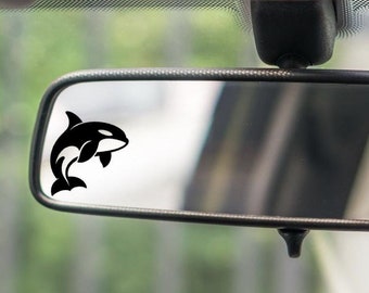 May include: A black and white orca silhouette sticker on a car's rearview mirror.