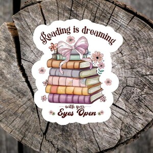 May include: A white sticker with a stack of books, a pink bow, and flowers. The text on the sticker reads "Reading is dreaming with your Eyes Open."