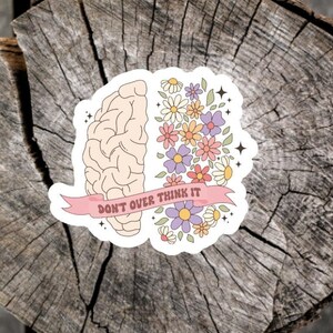 May include: A sticker with a brain on one side and flowers on the other. The brain is white and the flowers are pink, purple, and yellow. The sticker has the text "Don't over think it" on a pink ribbon.