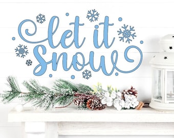 May include: A white wooden shelf displays a light blue "Let it Snow" sign with snowflake accents. A white lantern with star cutouts and winter greenery with pinecones complete the winter scene.