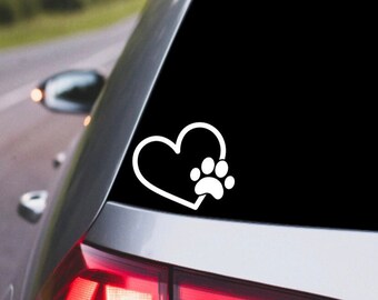 May include: White vinyl decal of a heart with a paw print inside. The decal is on the back window of a silver car.