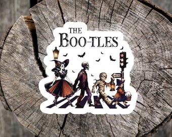 May include: A die-cut sticker featuring a Halloween-themed illustration of a witch, a skeleton, a mummy, and a small child walking across a crosswalk. The text THE BOO-TLES is printed above the figures, accompanied by bats, a street lamp, and a sign.