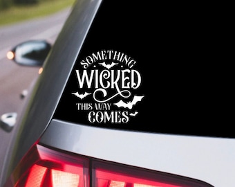 May include: A white vinyl decal with the text "Something Wicked This Way Comes" and bat silhouettes on a black background. The decal is applied to the back window of a silver car.