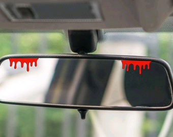 May include: A black rearview mirror with two red dripping paint decals on the top edge of the mirror.