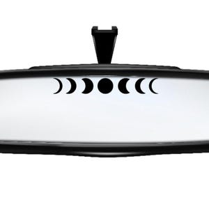 May include: A black rearview mirror with a moon phase decal. The decal features a crescent moon, a half moon, a full moon, a waning gibbous moon, and a waning crescent moon.