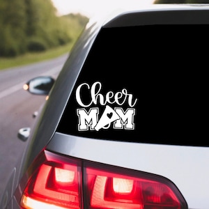 May include: White vinyl car decal with the text "Cheer Mom" in a stylized font. A white megaphone with a small heart is between the words "Mom".