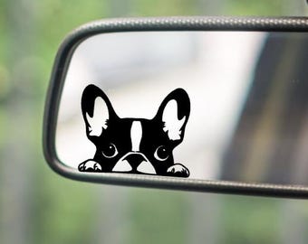 May include: A black and white vinyl decal of a French Bulldog face peeking over the bottom edge of a rectangular car side mirror. The dog has large upright ears, wide eyes, and a white stripe on its forehead, applied to the reflective glass surface.