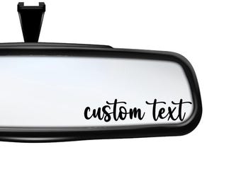 May include: A black rearview mirror with a white background and the text "custom text" in black cursive lettering.