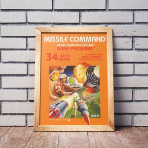 May include: A vintage poster for the Atari video game Missile Command. The poster is orange and features a cartoon illustration of a futuristic city under attack by missiles. The text on the poster reads "Missile Command", "Video Computer System", "Game Program", "34 Video Games", "Interplanetary Ballistic Missiles", and "Antiballistic Missiles".