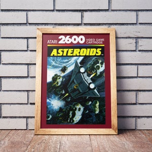 May include: A vintage Atari 2600 video game cartridge for the game Asteroids. The cartridge is red with white text and a picture of a spaceship flying through an asteroid field.