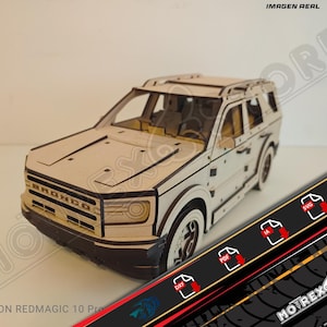 May include: A wooden model of a Bronco SUV, featuring detailed laser-cut construction. The model is primarily beige with black accents, including the Bronco logo on the front. The image includes the text "IMAGEN REAL" and "MOTREX STORE".
