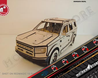 Può includere: Un modello in legno di un SUV Bronco, con una costruzione dettagliata tagliata al laser. Il modello è principalmente beige con dettagli neri, incluso il logo Bronco sulla parte anteriore. Il testo "IMAGEN REAL" e "MOTREX STORE" è incluso.