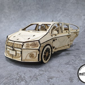 May include: A wooden model car kit of a Chevrolet Sonic, with the doors open, showing the interior details. The model is made of laser-cut wood and is ready to be assembled.