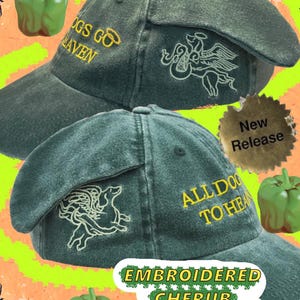 May include: Two green baseball caps with embroidered cherub weenie dogs. One cap has "DOGS GO TO HEAVEN" in yellow, the other says "ALL DOGS TO HEAVEN". A "New Release" sticker is visible.