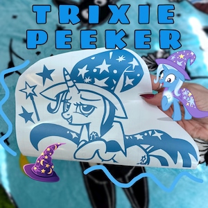 May include: A blue vinyl decal featuring a cartoon unicorn wearing a star-patterned wizard hat and cape. The design includes a star-topped wand and the text TRIXIE PEEKER in bold blue letters. The decal is shown on a white backing sheet.
