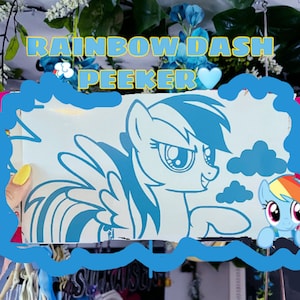 May include: A blue and white vinyl sticker featuring Rainbow Dash from My Little Pony. The sticker shows Rainbow Dash with her wings spread and a mischievous expression. The text "Rainbow Dash Peeker" is written above the sticker.