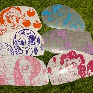 Pu&ograve; includere: Set di sei adesivi in ​​vinile termoadesivi con personaggi di My Little Pony. Gli adesivi sono su uno sfondo bianco con un motivo a griglia. I personaggi includono Pinkie Pie, Twilight Sparkle, Rainbow Dash, Fluttershy, Applejack e Rarity.