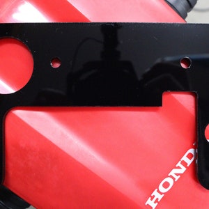 May include: Black metal motorcycle accessory plate with multiple holes and the text "LEHTOFF" printed on the right side.