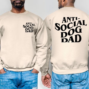 Pu&ograve; includere: Una felpa beige con la scritta "ANTI-SOCIAL DOG DAD" stampata in nero sul retro. Il testo &egrave; in un carattere in grassetto e stilizzato.