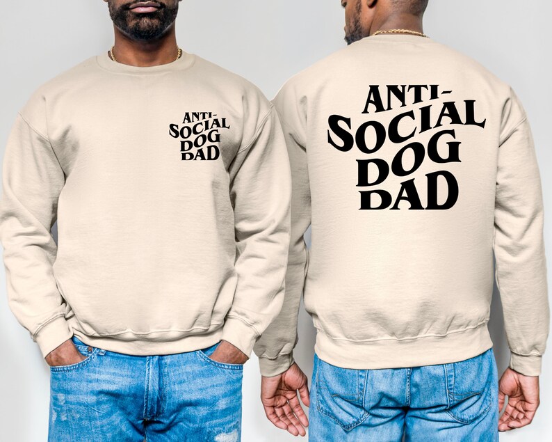 Pu&ograve; includere: Una felpa beige con la scritta "ANTI-SOCIAL DOG DAD" stampata in nero sul retro. Il testo &egrave; in un carattere in grassetto e stilizzato.