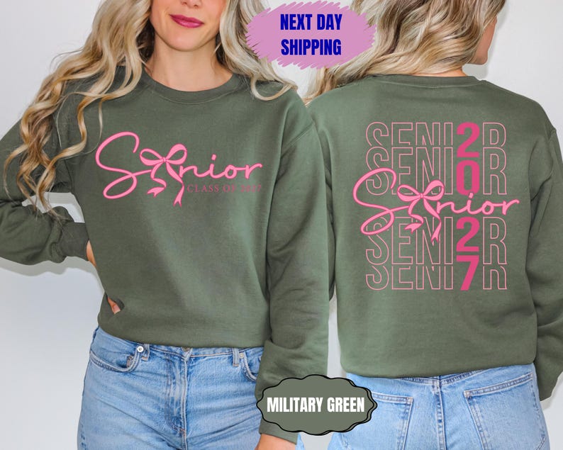 May include: Military green sweatshirt with the word "Senior" in pink script on the front, with a bow design. The back of the sweatshirt repeats "Senior 2027" in a stacked design. The sweatshirt is a crew neck style.