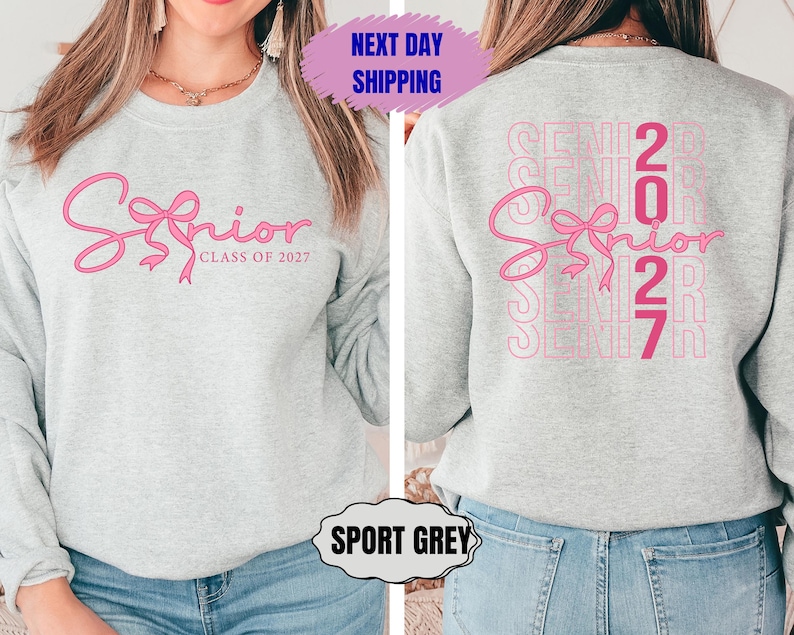 May include: A light gray sweatshirt with the word "Senior" in pink script with a bow design. The text "Class of 2027" is below. The back of the sweatshirt has the word "Senior" and the number "2027" repeated in a vertical pattern.
